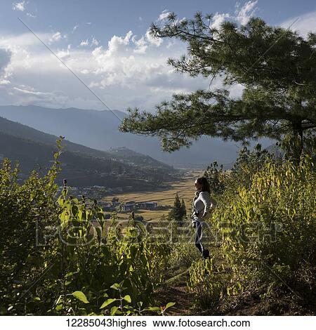 Stock Photograph - A woman stands looking out over Paro Valley; Paro, Bhutan. Fotosearch