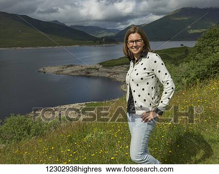 A woman stands on a slope of wildflowers and grass overlooking tranquil water and mountains; Scotland View Large Photo Image Stock Photograph - A woman stands on a slope of wildflowers and grass overlooking tranquil water and mountains; Scotland. Fotosearch