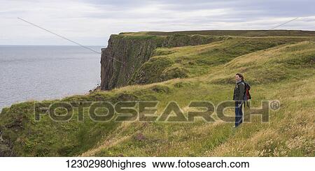 Stock Photograph - A woman stands on grass near a ridge overlooking Duncansby Head; John O'Groats, Scotland. Fotosearch