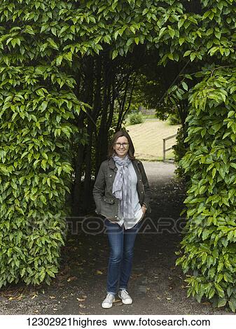 Stock Photograph - A woman stands posing in a foliage covered entrance to a walkway at Dunrobin Castle; Golspie, Scotland. Fotosearch