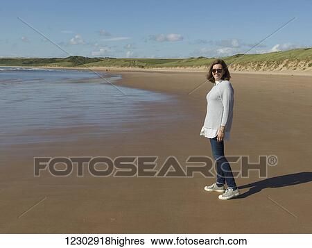 Stock Photograph - A woman wearing sunglasses standing on Cruden Bay Beach on Cruden Bay; Aberdeenshire, Scotland. Fotosearch