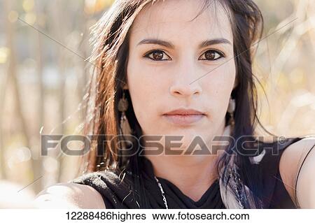 Stock Photograph - A young aboriginal female model looks at the camera in a concentrated stern gaze taking a selfie up close; Vancouver, British Columbia, Canada. Fotosearch