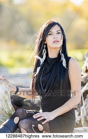 A young aboriginal female model looks at the camera in a concentrated fashion pose sitting on logs in the outdoors in autumn; Vancouver, British Columbia, Canada View Large Photo Image Stock Photograph - A young aboriginal female model looks at the camera in a concentrated fashion pose sitting on logs in the outdoors in autumn; Vancouver, British Columbia, Canada. Fotosearch