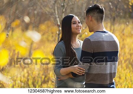 Stock Photograph - A young Asian couple enjoying a romantic time together outdoors in a park in autumn and embracing each other in the warmth of the sunlight during the early evening; Edmonton, Alberta, Canada. Fotosearch
