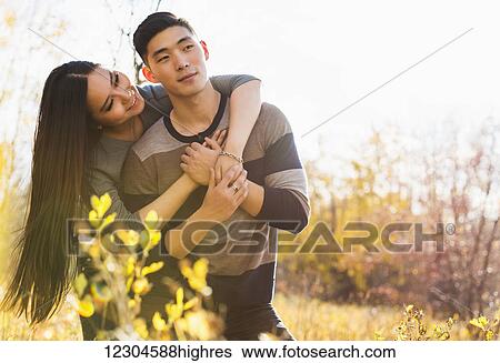 Stock Photograph - A young Asian couple enjoying a romantic time together outdoors in a park in autumn and embracing each other in the warmth of the sunlight during the early evening; Edmonton, Alberta, Canada. Fotosearch