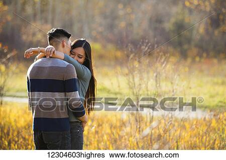 A young Asian couple enjoying a romantic time together outdoors in a park in autumn and embracing each other in the warmth of the sunlight during the early evening; Edmonton, Alberta, Canada View Large Photo Image Stock Photograph - A young Asian couple enjoying a romantic time together outdoors in a park in autumn and embracing each other in the warmth of the sunlight during the early evening; Edmonton, Alberta, Canada. Fotosearch
