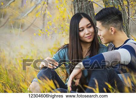 A young Asian couple enjoying a romantic time together outdoors in a park in autumn sitting under a tree and looking into each other's eyes; Edmonton, Alberta, Canada View Large Photo Image Stock Photograph - A young Asian couple enjoying a romantic time together outdoors in a park in autumn sitting under a tree and looking into each other's eyes; Edmonton, Alberta, Canada. Fotosearch