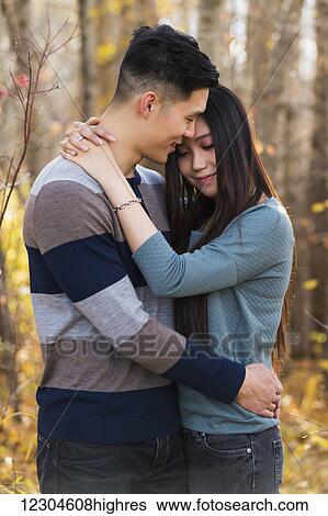 Stock Photograph - A young Asian couple enjoying a romantic time together outdoors in a park in autumn and embracing each other in the warmth of the sunlight; Edmonton, Alberta, Canada. Fotosearch