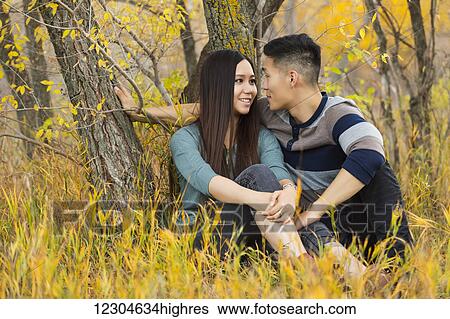 A young Asian couple enjoying a romantic time together and sitting under a tree in a park in autumn; Edmonton, Alberta, Canada View Large Photo Image Stock Photograph - A young Asian couple enjoying a romantic time together and sitting under a tree in a park in autumn; Edmonton, Alberta, Canada. Fotosearch