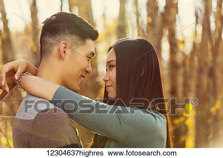 Stock Photograph - A young Asian couple enjoying a romantic time together outdoors in a park in autumn and embracing each other in the warmth of the sunlight during the early evening; Edmonton, Alberta, Canada. Fotosearch