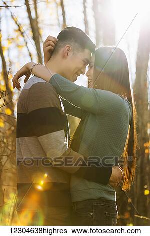 Stock Photograph - A young Asian couple enjoying a romantic time together outdoors in a park in autumn and embracing each other in the warmth of the sunlight during the early evening; Edmonton, Alberta, Canada. Fotosearch