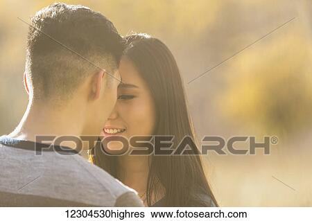 Stock Photograph - A young Asian couple enjoying quality time together in a park in autumn and embracing each other in the warmth of the evening sunlight; Edmonton, Alberta, Canada. Fotosearch