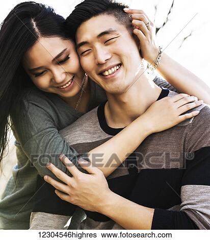 Stock Photograph - A young Asian couple enjoying quality time together outdoors in a park in autumn and embracing each other in the warmth of the sunlight during the early evening; Edmonton, Alberta, Canada. Fotosearch