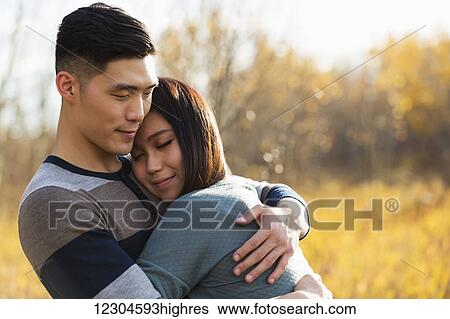 A young Asian couple enjoying quality time together outdoors in a park in autumn and embracing each other in the warmth of the sunlight during the early evening; Edmonton, Alberta, Canada View Large Photo Image Stock Photograph - A young Asian couple enjoying quality time together outdoors in a park in autumn and embracing each other in the warmth of the sunlight during the early evening; Edmonton, Alberta, Canada. Fotosearch