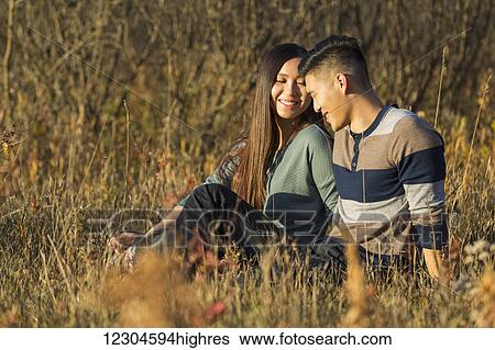Stock Photograph - A young Asian couple enjoying quality time together outdoors in a park in autumn in the warmth of the sunlight during the early evening; Edmonton, Alberta, Canada. Fotosearch