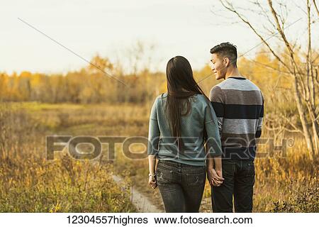 A young Asian couple holding hands while walking in a park in autumn and and enjoying the warmth of the evening sunshine; Edmonton, Alberta, Canada View Large Photo Image Stock Photograph - A young Asian couple holding hands while walking in a park in autumn and and enjoying the warmth of the evening sunshine; Edmonton, Alberta, Canada. Fotosearch