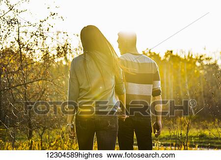 Stock Photograph - A young Asian couple holding hands while walking in a park in autumn and enjoying the warmth of the sunlight during the early evening; Edmonton, Alberta, Canada. Fotosearch
