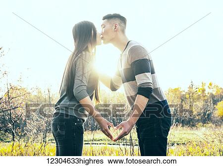 A young Asian couple kissing in a park in autumn and making a heart with their hands in the warmth of the setting sun; Edmonton, Alberta, Canada View Large Photo Image Stock Photograph - A young Asian couple kissing in a park in autumn and making a heart with their hands in the warmth of the setting sun; Edmonton, Alberta, Canada. Fotosearch