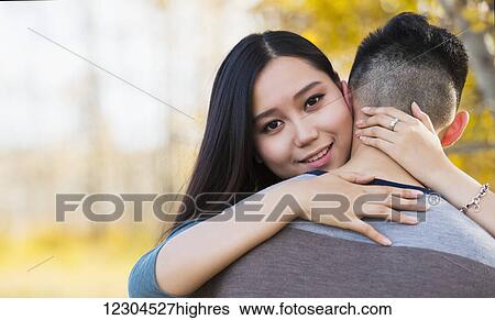A young Asian woman hugging her boyfriend and looking over his shoulder at the camera in a park during autumn; Edmonton, Alberta, Canada View Large Photo Image Stock Photograph - A young Asian woman hugging her boyfriend and looking over his shoulder at the camera in a park during autumn; Edmonton, Alberta, Canada. Fotosearch