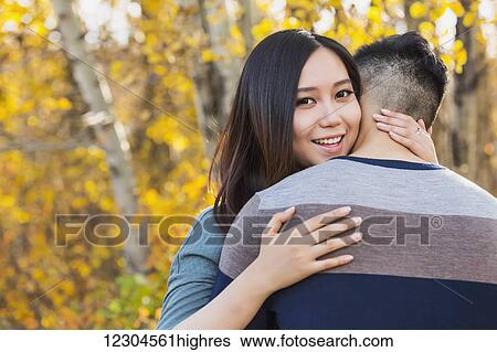 A young Asian woman hugging her boyfriend in a park in autumn and looking over his shoulder at the camera; Edmonton, Alberta, Canada View Large Photo Image Stock Photograph - A young Asian woman hugging her boyfriend in a park in autumn and looking over his shoulder at the camera; Edmonton, Alberta, Canada. Fotosearch