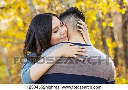 A young Asian woman hugging her boyfriend in a park in autumn and looking over his shoulder at the camera; Edmonton, Alberta, Canada View Large Photo Image Stock Photograph - A young Asian woman hugging her boyfriend in a park in autumn and looking over his shoulder at the camera; Edmonton, Alberta, Canada. Fotosearch