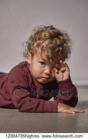A young child with blond curly hair lays on the floor rubbing his eyes with fatigue; Hamilton, Ontario, Canada View Large Photo Image Stock Photograph - A young child with blond curly hair lays on the floor rubbing his eyes with fatigue; Hamilton, Ontario, Canada. Fotosearch