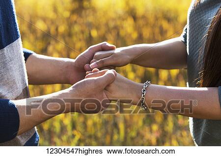 Stock Photograph - A young couple enjoying quality time together outdoors in a park in autumn and holding hands in the warmth of the sunlight during the early evening; Edmonton, Alberta, Canada. Fotosearch