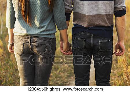 Stock Photograph - A young couple holding hands while walking in a park in autumn and and enjoying the warmth of the evening sunshine; Edmonton, Alberta, Canada. Fotosearch