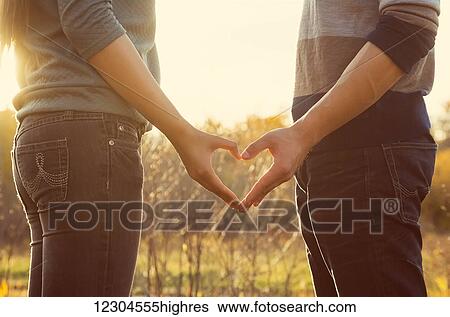 A young couple standing in a park in autumn and making a heart with their hands in the warmth of the setting sun; Edmonton, Alberta, Canada View Large Photo Image Stock Photograph - A young couple standing in a park in autumn and making a heart with their hands in the warmth of the setting sun; Edmonton, Alberta, Canada. Fotosearch