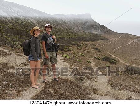 A young couple stands on a rugged dirt trail on a mountainous landscape looking out; Praia da Cordoama, Portugal View Large Photo Image Stock Photograph - A young couple stands on a rugged dirt trail on a mountainous landscape looking out; Praia da Cordoama, Portugal. Fotosearch