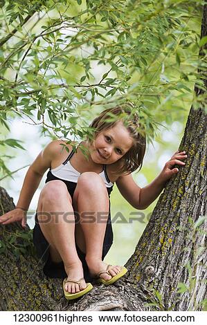 Stock Photograph - A young girl climbing in a tree in a park; Edmonton, Alberta, Canada. Fotosearch