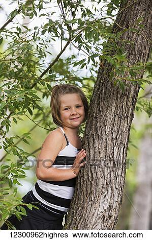 Stock Photograph - A young girl climbing in a tree in a park; Edmonton, Alberta, Canada. Fotosearch