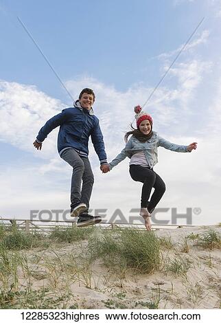 A young man and woman leaping on a beach while holding hands; Tarifa, Cadiz, Andalusia, Spain View Large Photo Image Stock Photograph - A young man and woman leaping on a beach while holding hands; Tarifa, Cadiz, Andalusia, Spain. Fotosearch