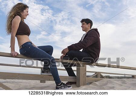 A young man and woman sit talking on a wooden fence at the beach; Tarifa, Cadiz, Andalusia, Spain View Large Photo Image Stock Photograph - A young man and woman sit talking on a wooden fence at the beach; Tarifa, Cadiz, Andalusia, Spain. Fotosearch