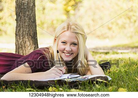 Stock Photograph - A young woman doing homework outdoors while enjoying a warm autumn day in a park and posing for the camera; Edmonton, Alberta, Canada. Fotosearch