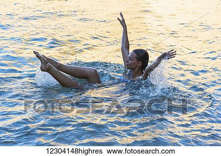 Stock Photograph - A young woman in the water with her torso immersed and her arms and legs above the water, exercising; Tarifa, Cadiz, Andalusia, Spain. Fotosearch