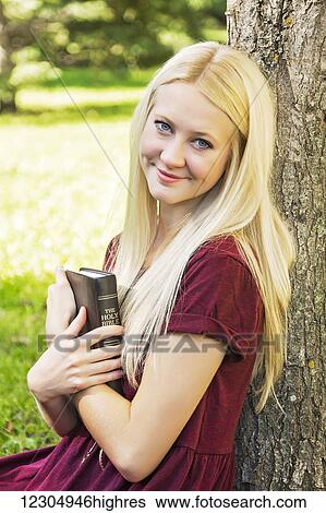 A young woman with long blond hair holding her Bible close to her chest while spending personal devotional time outdoors in a park in autumn; Edmonton, Alberta, Canada View Large Photo Image Stock Photograph - A young woman with long blond hair holding her Bible close to her chest while spending personal devotional time outdoors in a park in autumn; Edmonton, Alberta, Canada. Fotosearch