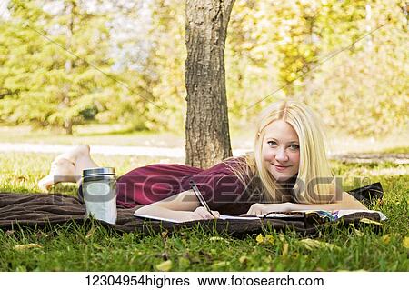 A young woman with long blond hair doing homework outdoors while enjoying a warm autumn day in a park and posing for the camera; Edmonton, Alberta, Canada View Large Photo Image Stock Photograph - A young woman with long blond hair doing homework outdoors while enjoying a warm autumn day in a park and posing for the camera; Edmonton, Alberta, Canada. Fotosearch