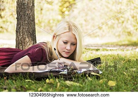 Stock Photograph - A young woman with long blond hair doing homework outdoors while enjoying a warm autumn day in a park; Edmonton, Alberta, Canada. Fotosearch