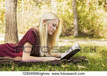 Stock Photograph - A young woman with long blond hair spending personal time in Bible study outdoors in a park in autumn; Edmonton, Alberta, Canada. Fotosearch