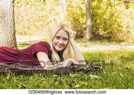 Stock Photograph - A young woman with long blond hair doing homework outdoors while enjoying a warm autumn day in a park and posing for the camera; Edmonton, Alberta, Canada. Fotosearch