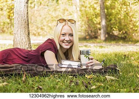 Stock Photograph - A young woman with long blond hair spending personal time in Bible study outdoors in a park in autumn and posing for the camera; Edmonton, Alberta, Canada. Fotosearch