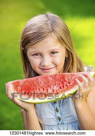 Stock Photograph - Adorable cute little girl eating watermelon on the grass in summertime. Fotosearch