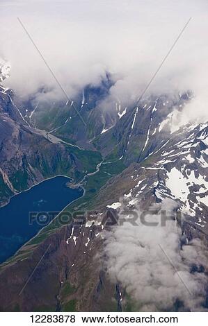 Stock Photo - Aerial view of clouds obscuring peaks with a lush green valley and lake visible in the foreground, Aleutian Range, Alaska Peninsula, Southwestern Alaska, USA, Summer. Fotosearch