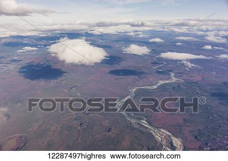 Stock Photograph - Aerial view of patchy clouds above a tundra landscape, a river cutting through the foreground; Alaska, United States of America. Fotosearch