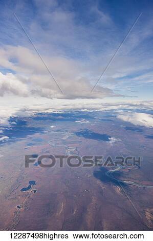 Stock Photograph - Aerial view of patchy clouds above a tundra landscape, a river cutting through the foreground; Alaska, United States of America. Fotosearch