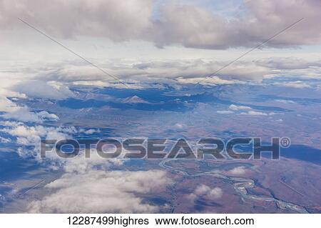 Stock Photograph - Aerial view of patchy clouds above a tundra landscape, a river cutting through the foreground; Alaska, United States of America. Fotosearch