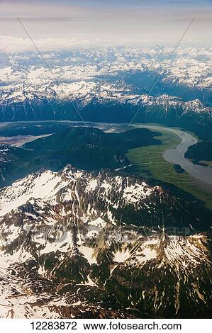 Stock Image - Aerial view of snow-capped peaks surrounding a green river valley, Aleutian Range, Alaska Peninsula, Southwestern Alaska, USA, Summer. Fotosearch