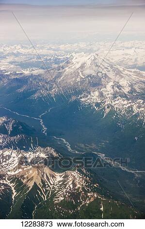 Stock Image - Aerial view of snow-capped peaks surrounding a green river valley, Aleutian Range, Alaska Peninsula, Southwestern Alaska, USA, Summer. Fotosearch