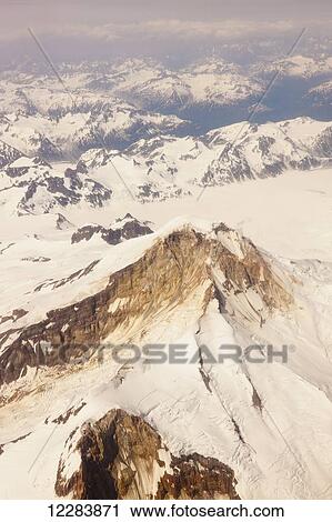 Stock Image - Aerial view of snow-covered mountains and bare rock peaks of the Aleutian Range, Alaska Peninsula, Southwestern Alaska, USA, Summer. Fotosearch